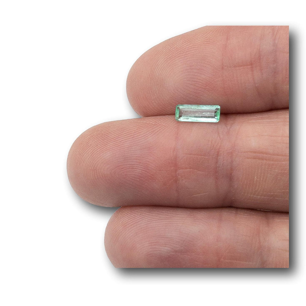 0.45ct long emerald-cut Muzo Colombian emerald gemstone held on a finger.