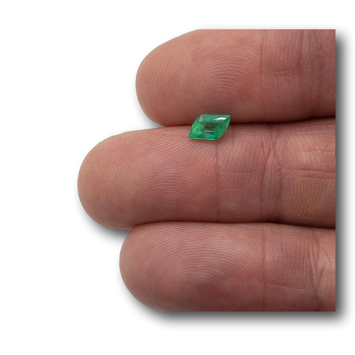 0.58ct step-cut rhomboid Muzo emerald with a vibrant green hue held between fingers.