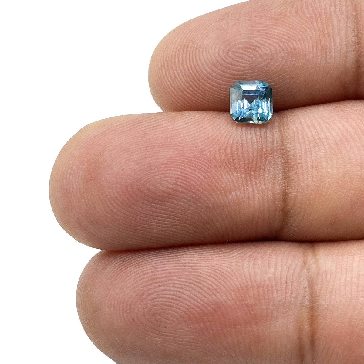 0.79ct asscher cut blue Montana sapphire held between fingers, showcasing its square shape and faceted blue gemstone surface.