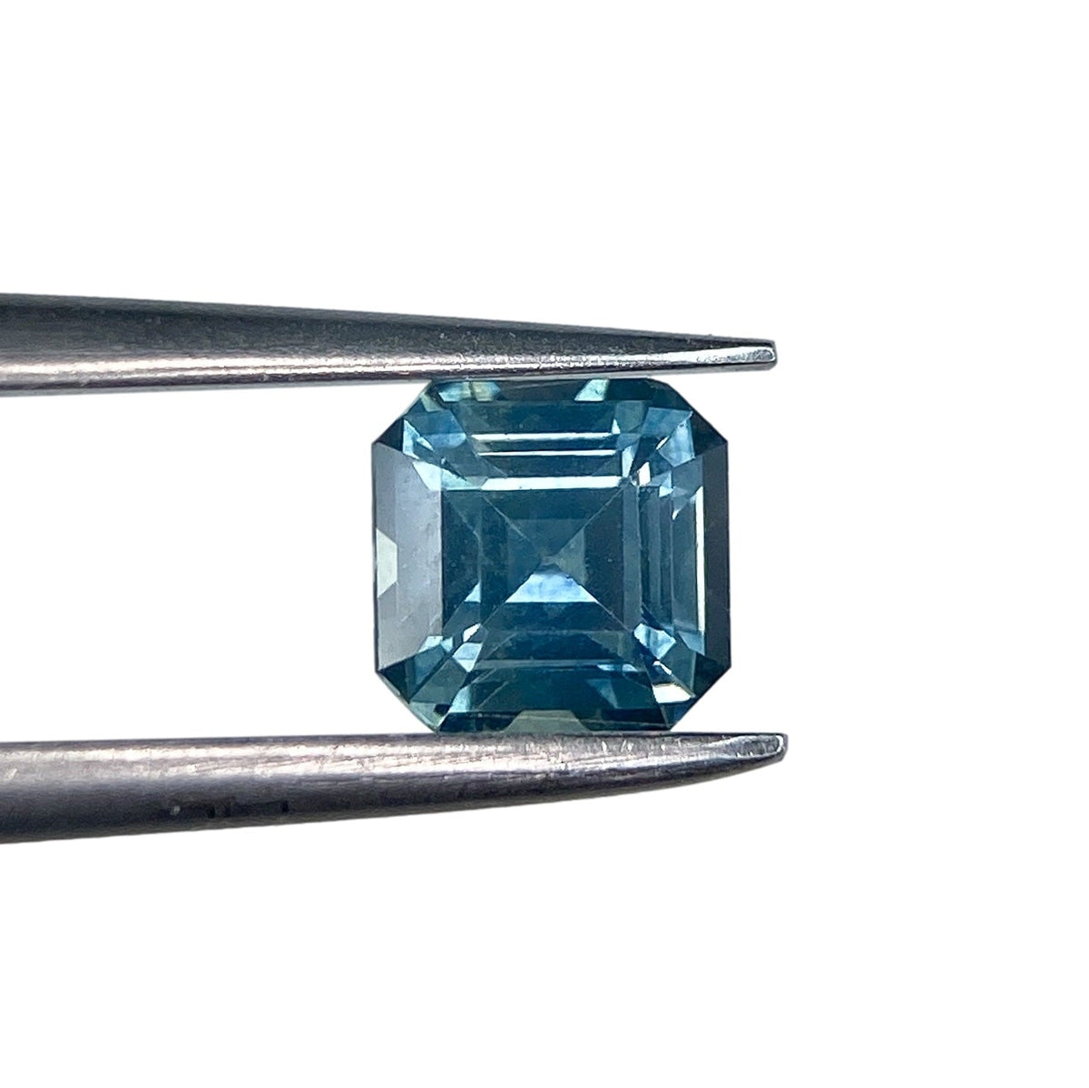 0.79ct asscher cut blue Montana sapphire held in metal tweezers against a white background.