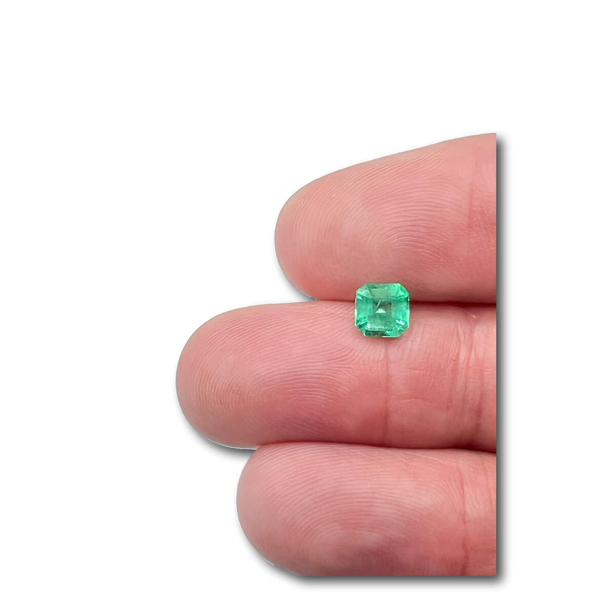 Radiant cut Muzo Colombian emerald gemstone with a vibrant green hue held between fingers.