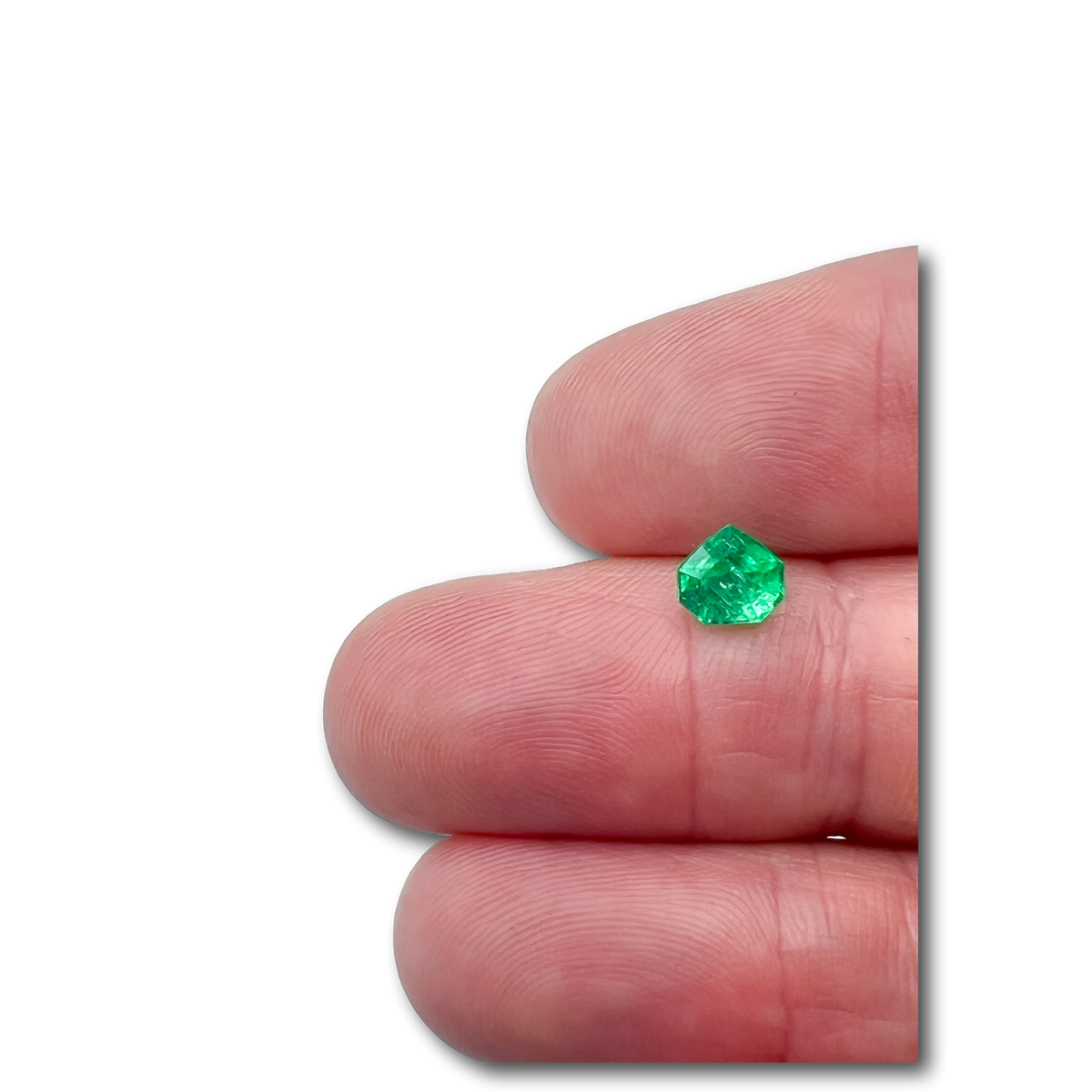 0.90ct Muzo origin emerald with a step-cut shield shape held between fingers.