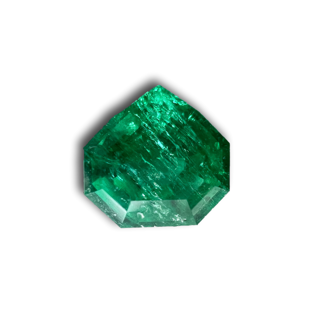 0.90ct Muzo origin emerald with a step-cut shield shape and vibrant green color against a white background.