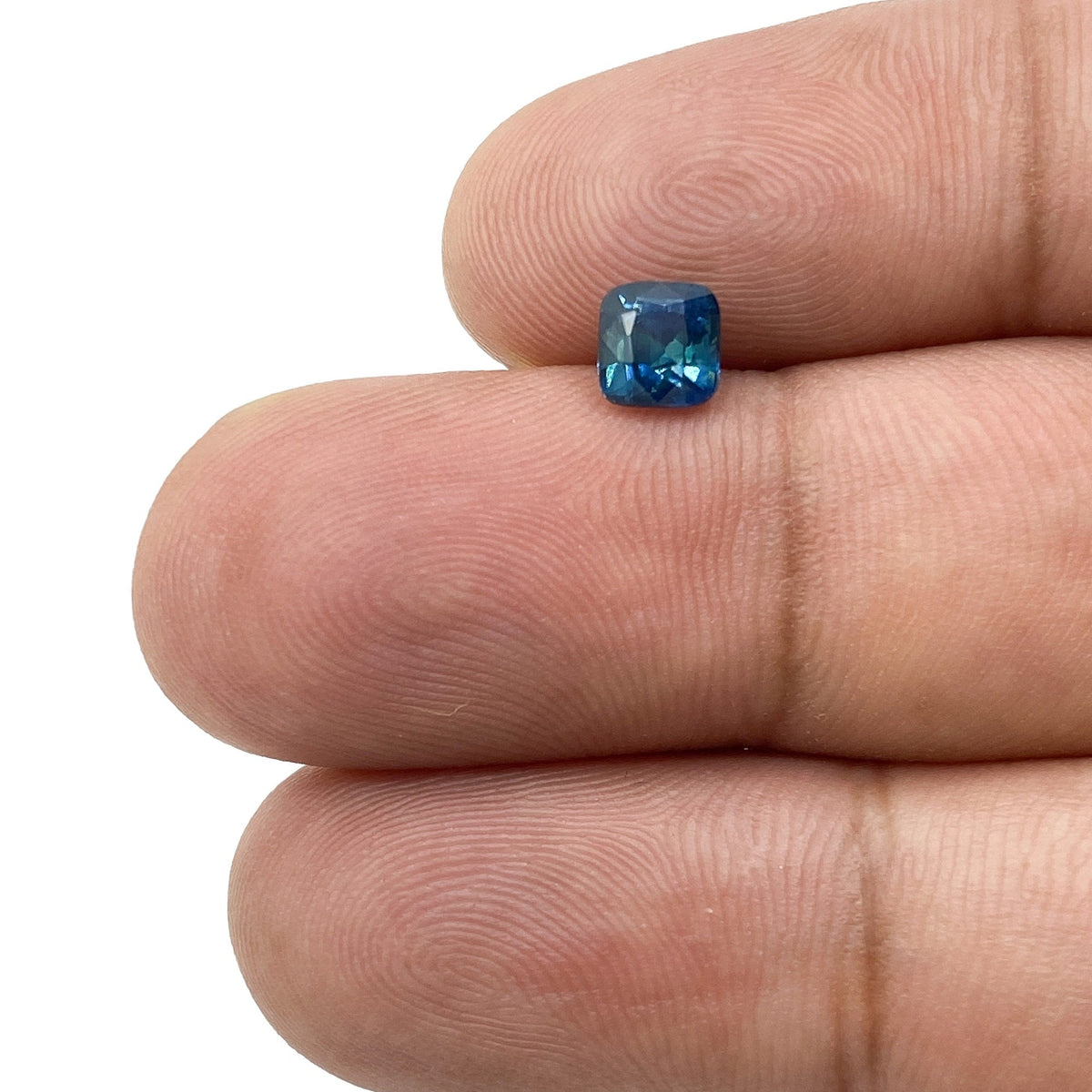 0.91ct brilliant cut cushion-shaped blue Montana sapphire held between two fingers.