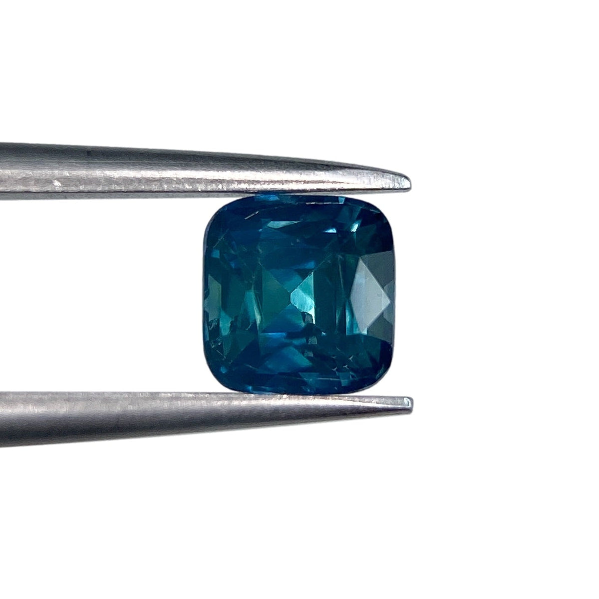 0.91ct brilliant cut cushion-shaped blue Montana sapphire held in metal tweezers against a white background.