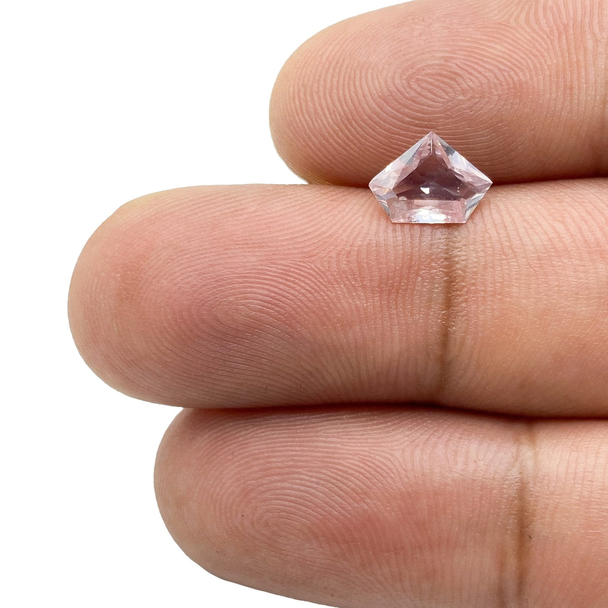 0.91ct brilliant cut pink sapphire with a unique shield shape held between fingers.