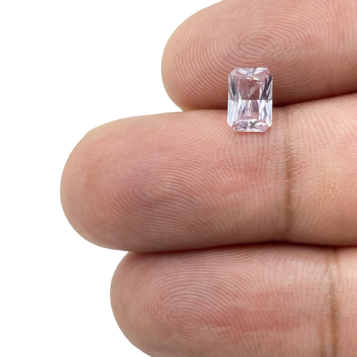 0.92ct radiant cut pink sapphire gemstone held between fingers, showcasing its rectangular shape and light pink hue.