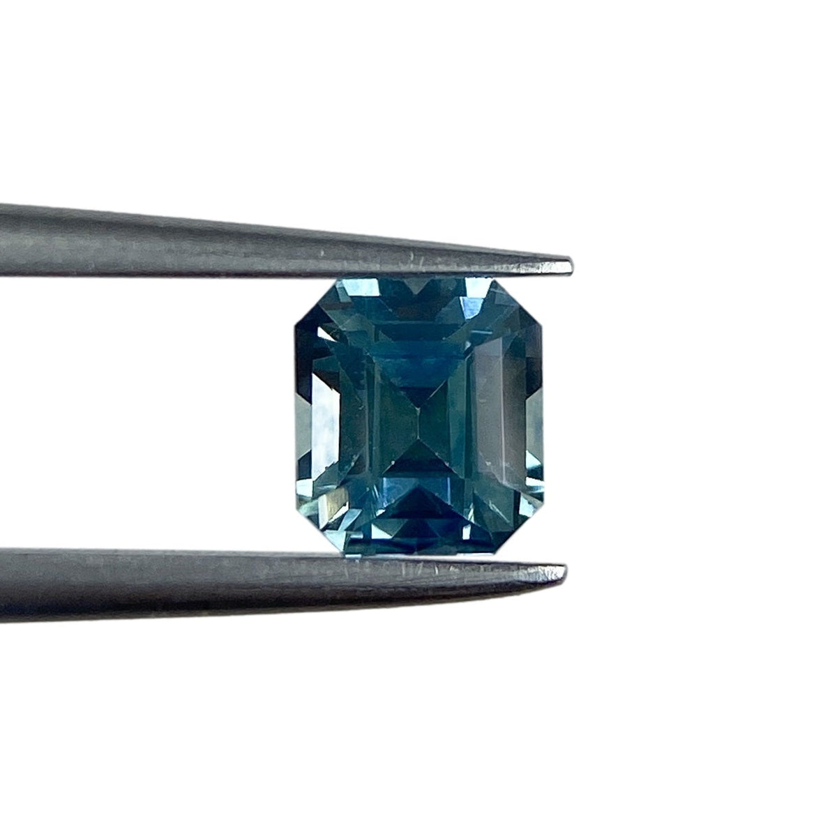 0.94ct Asscher cut blue Montana sapphire held in metal tweezers against a white background.