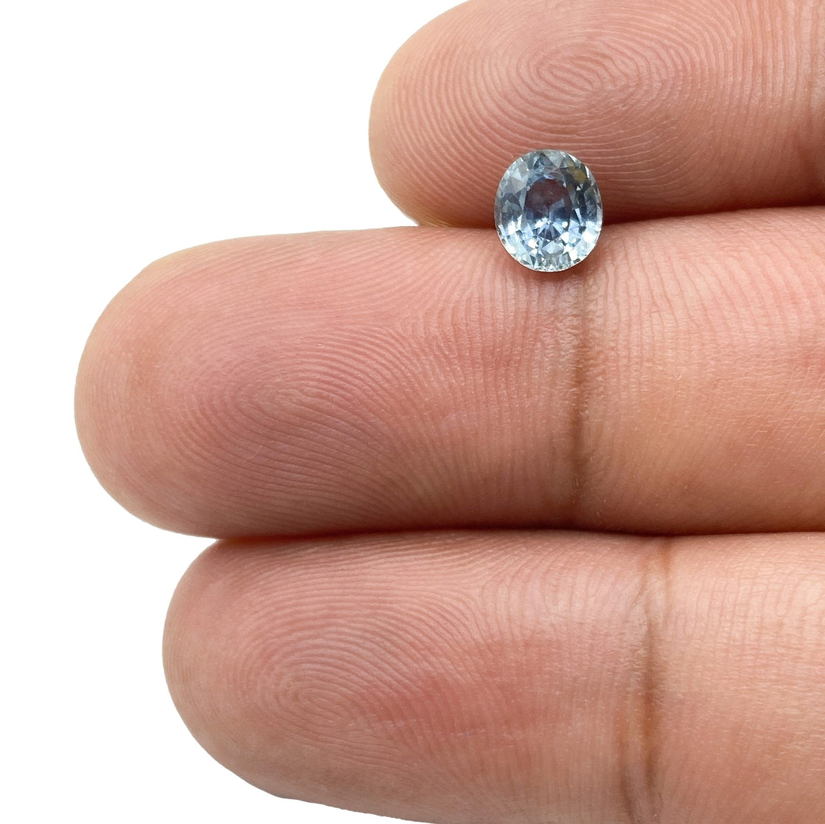 0.97ct oval brilliant cut blue Montana sapphire held between fingers, showcasing its light blue color and faceted sparkle.