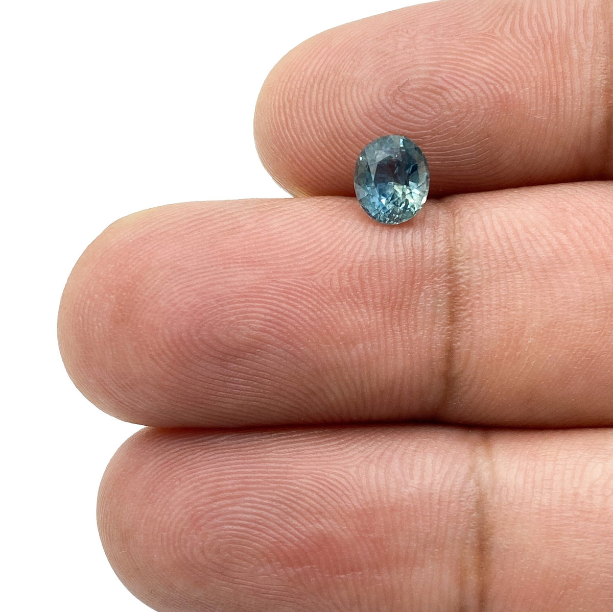 0.97ct oval brilliant cut blue Montana sapphire held between fingers, showcasing its faceted gemstone clarity.