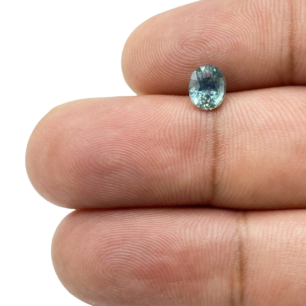0.97ct oval brilliant cut blue Montana sapphire held between fingers, showcasing its faceted gemstone clarity.