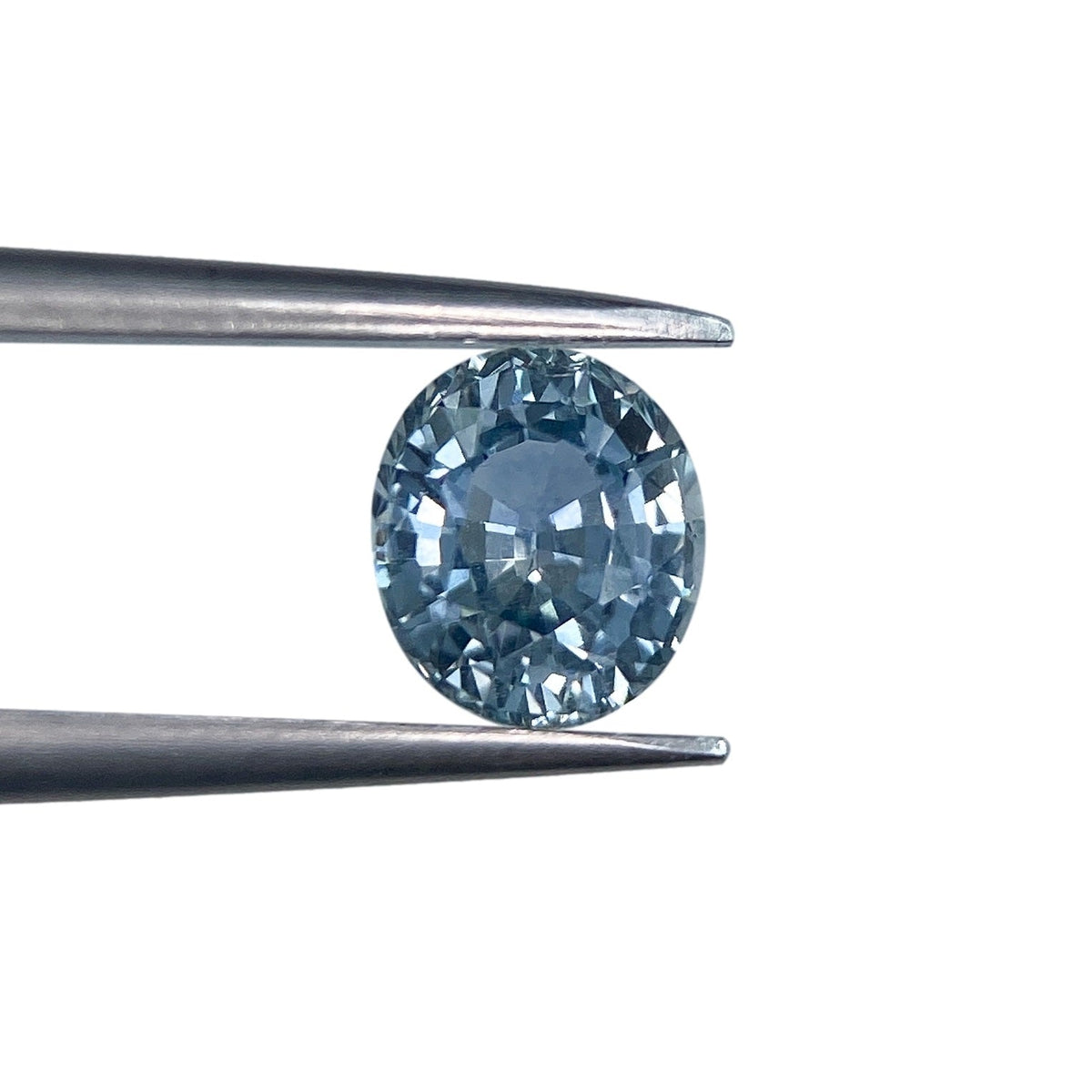 0.97ct oval brilliant cut blue Montana sapphire held in metal tweezers against a white background.