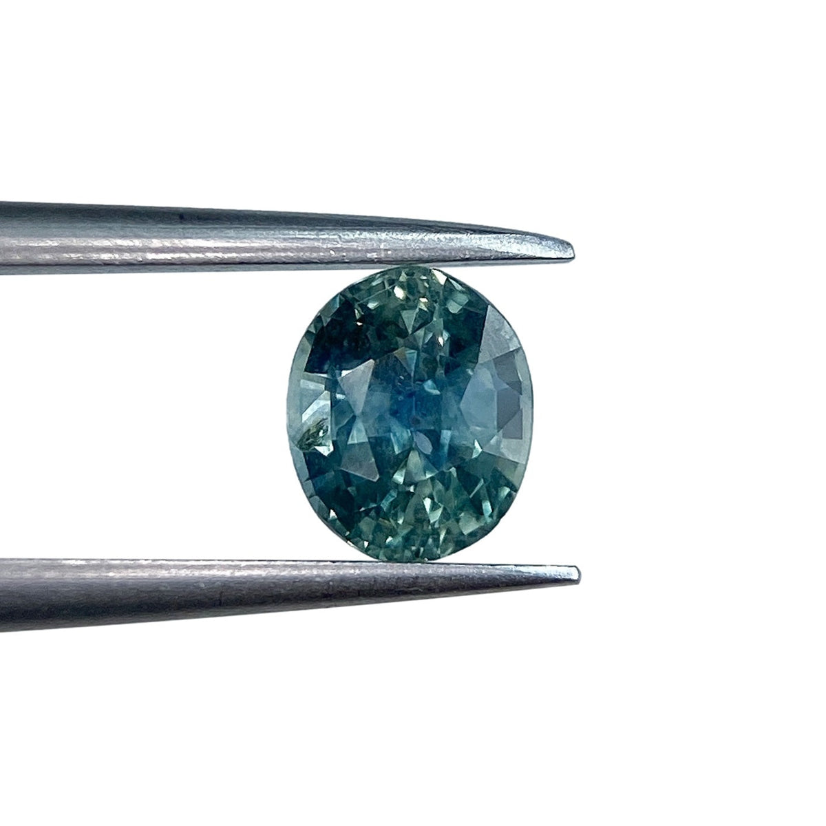 0.97ct oval brilliant cut blue Montana sapphire held in metal tweezers against a white background.