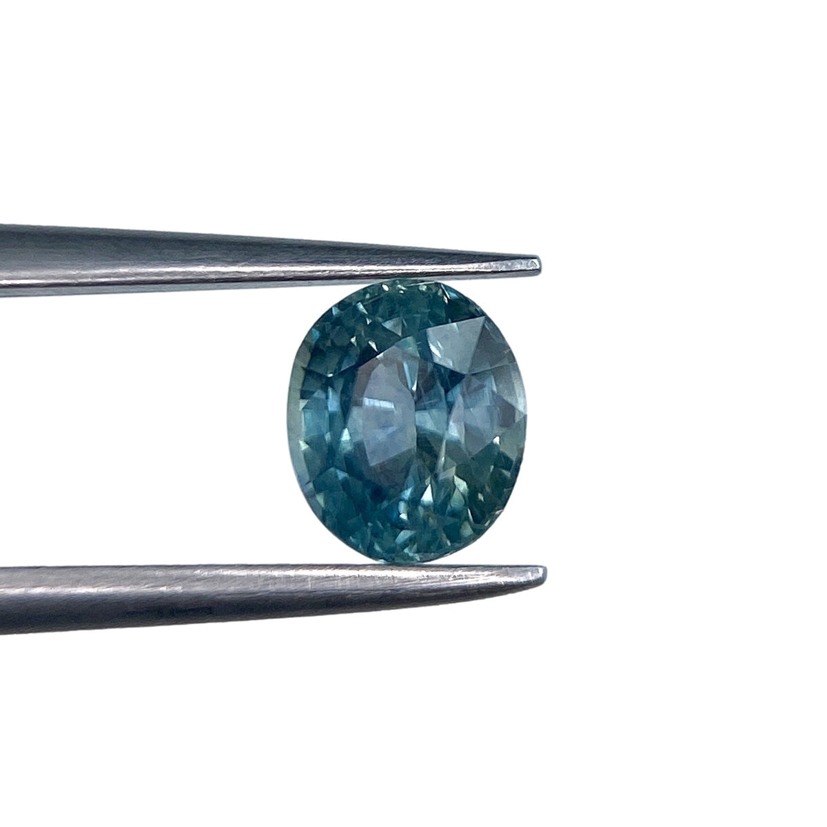 0.97ct oval brilliant cut blue Montana sapphire held in metal tweezers against a white background.