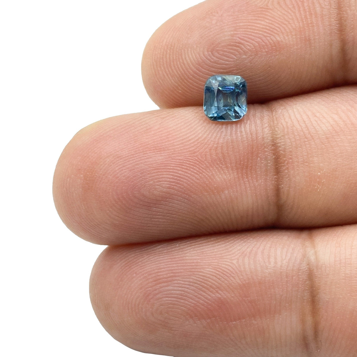 0.98ct brilliant cut cushion-shaped blue Montana sapphire held between fingers.