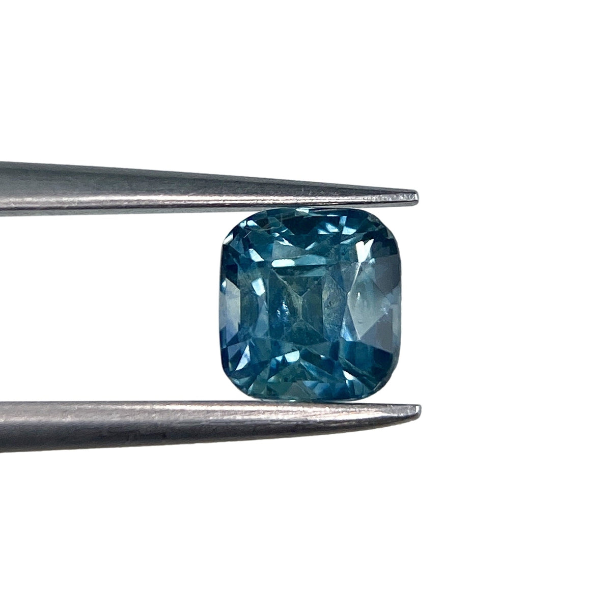 0.98ct cushion-cut blue Montana sapphire held in metal tweezers against a white background.