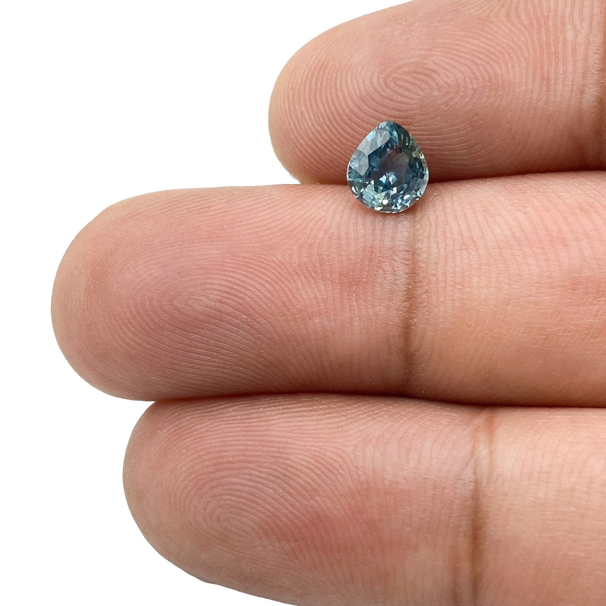 0.98ct pear-shaped blue Montana sapphire with a brilliant cut held between fingers.