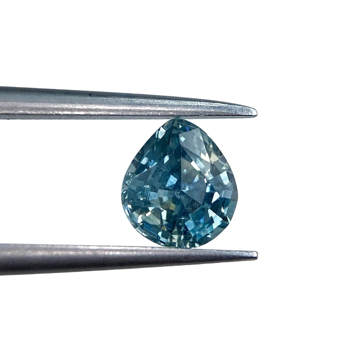 0.98ct pear-shaped blue Montana sapphire with a brilliant cut held in metal tweezers against a white background.