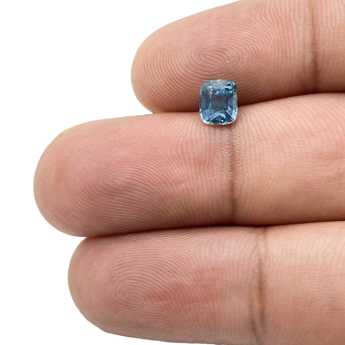 0.99ct brilliant cut cushion-shaped blue Montana sapphire held between two fingers.