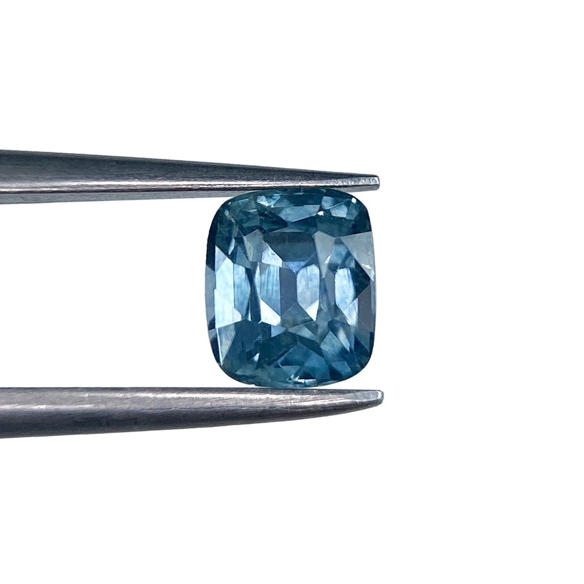 0.99ct cushion-cut blue Montana sapphire with a brilliant facet pattern held in metal tweezers.
