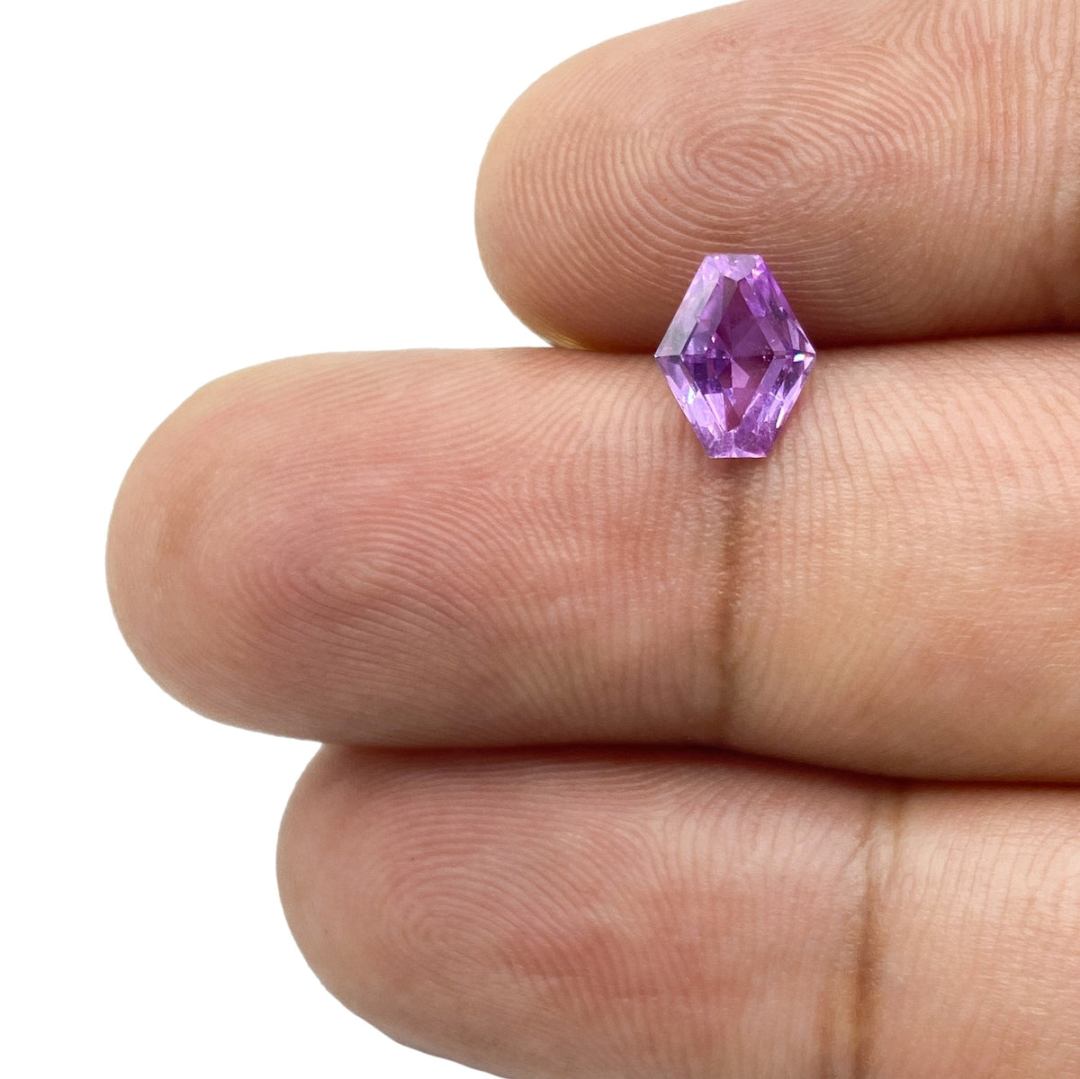 1.00ct brilliant cut violet sapphire in a unique lozenge shape held between fingers against a white background.