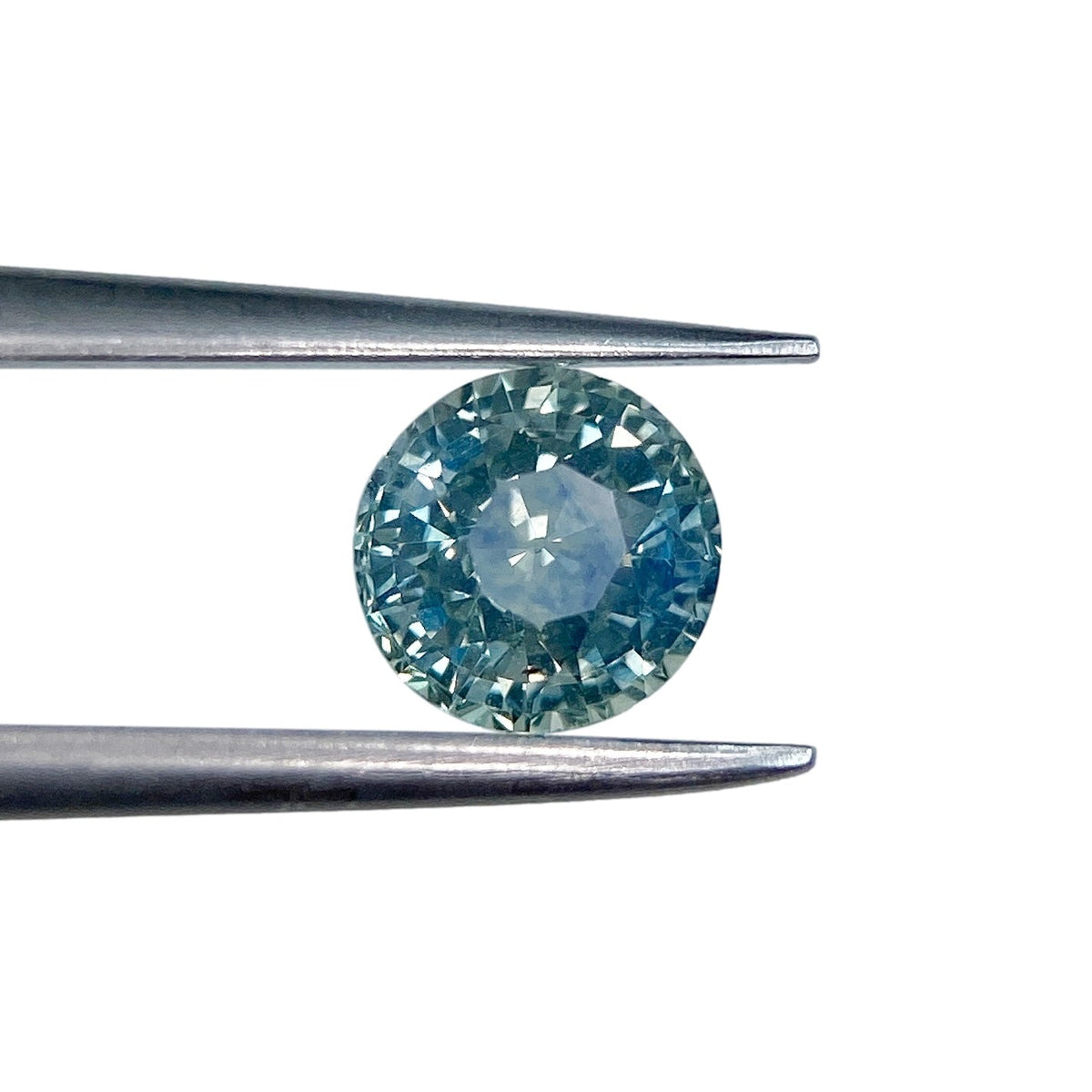 1.01ct round brilliant cut blue Montana sapphire held in metal tweezers against a white background.