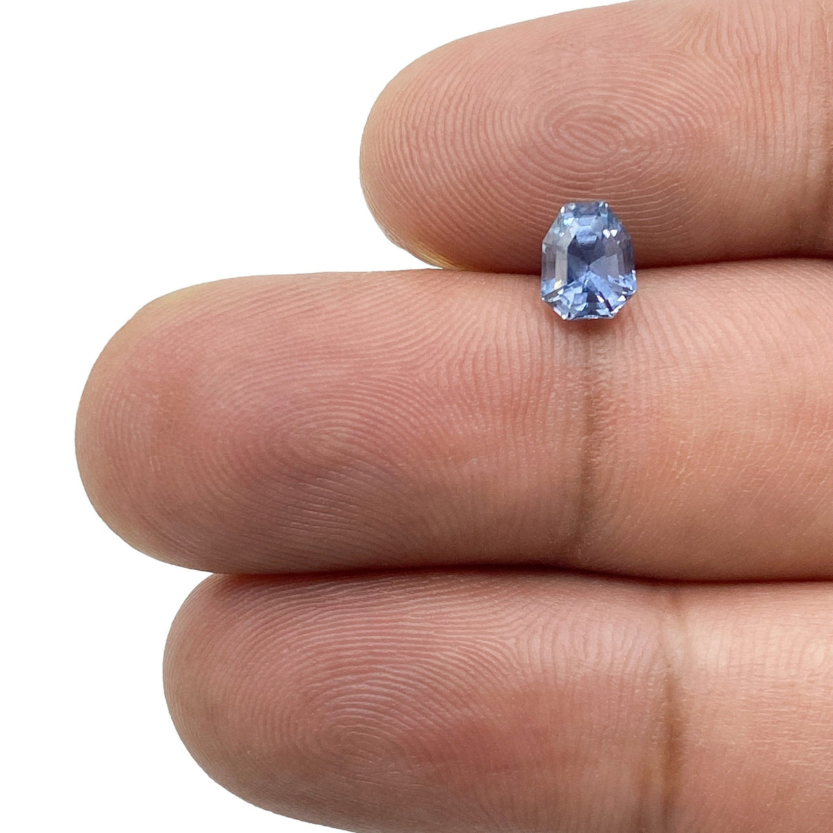 1.01ct shield-shaped blue sapphire with a step cut held between fingers.