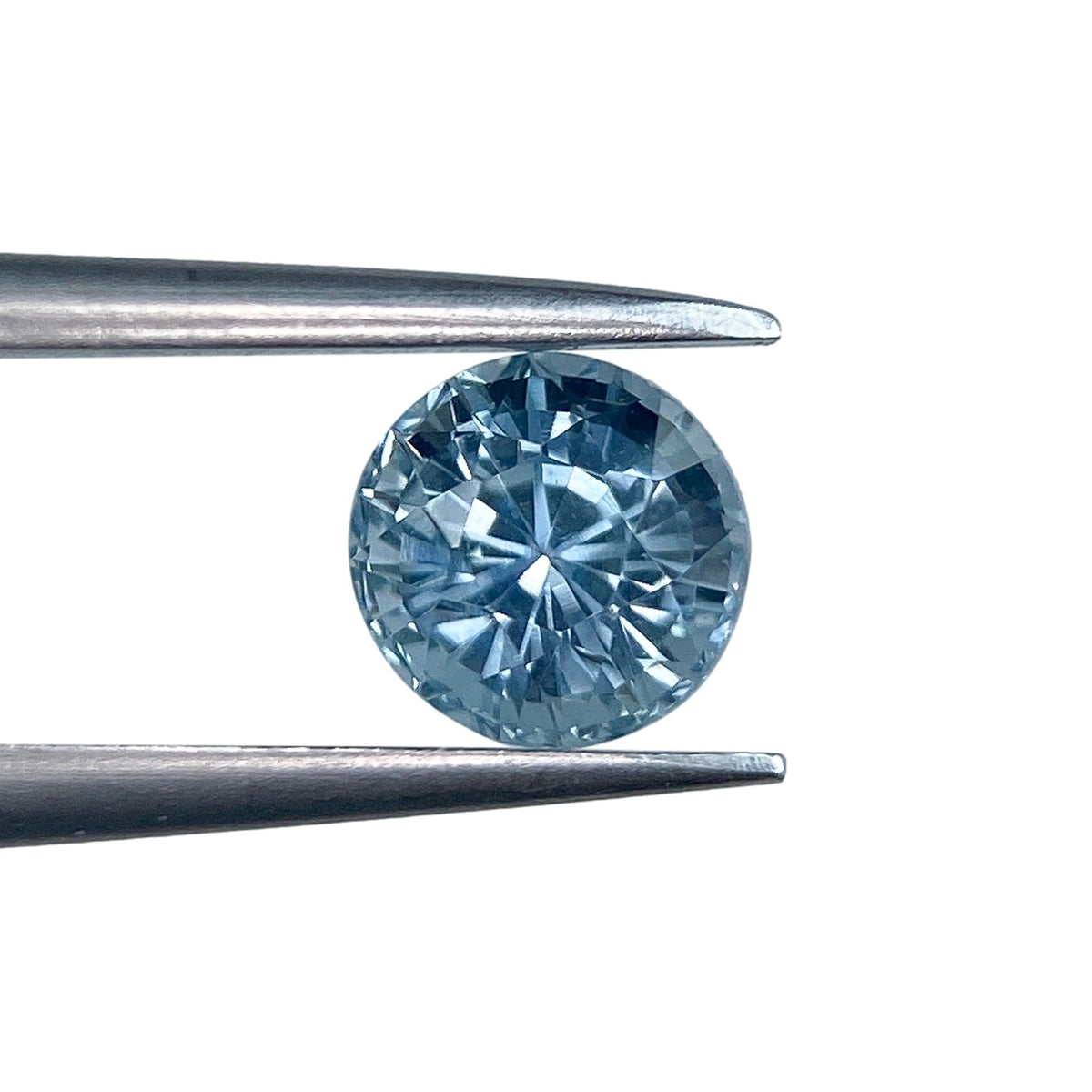 1.02ct round brilliant cut blue Montana sapphire held in metal tweezers against a white background.