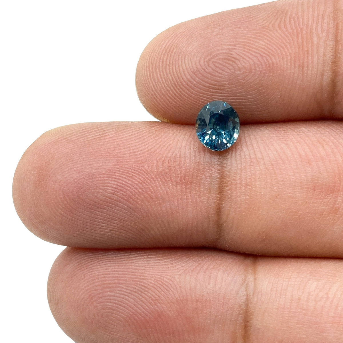 1.03ct oval brilliant cut blue Montana sapphire held between fingers.