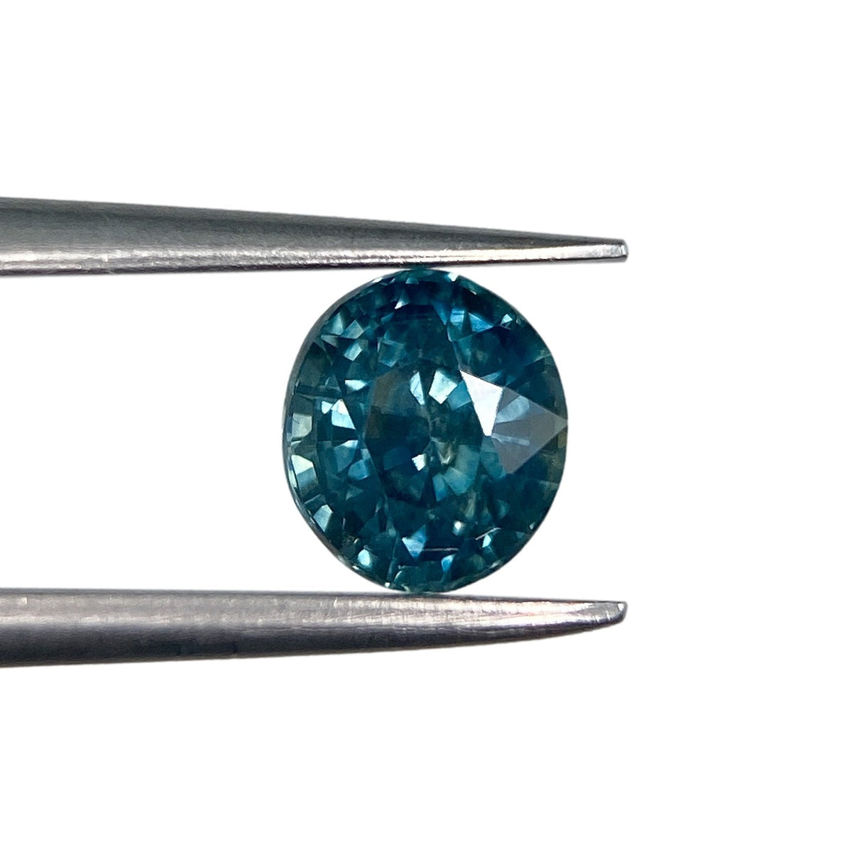 1.03ct oval brilliant cut blue Montana sapphire held in metal tweezers against a white background.