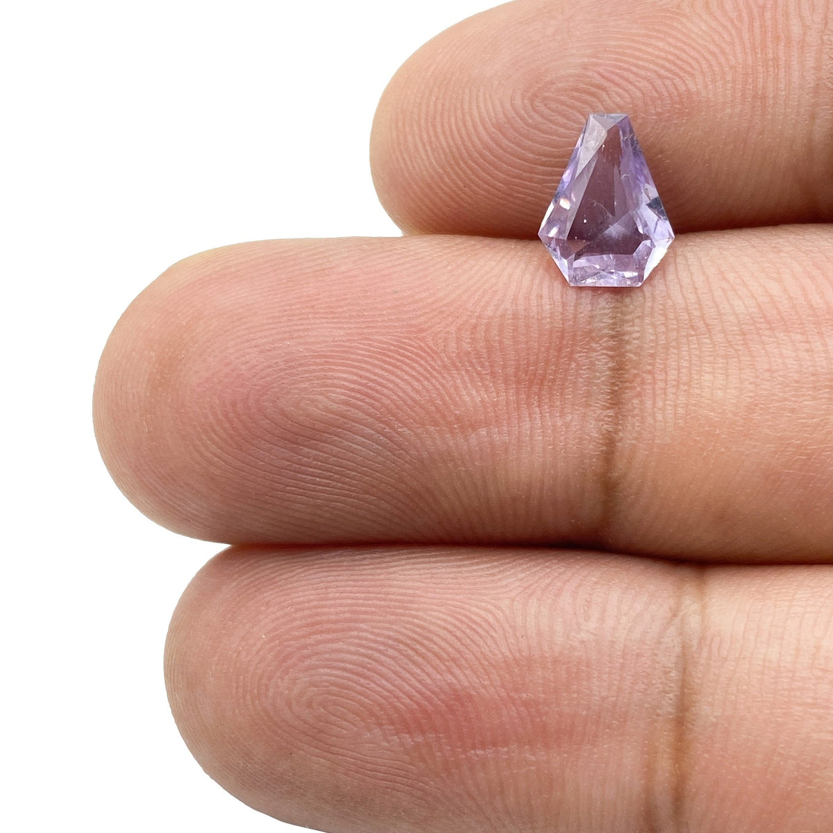 1.03ct brilliant cut shield-shaped pink sapphire held between fingers.