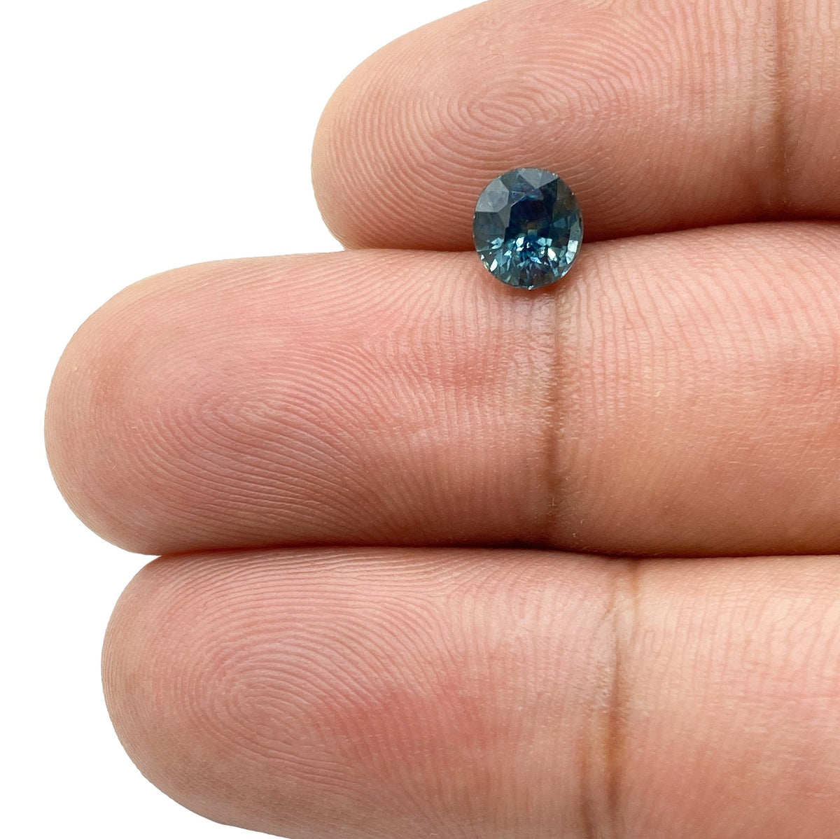1.04ct oval brilliant cut blue Montana sapphire held between two fingers, showcasing deep blue tones and faceted clarity.