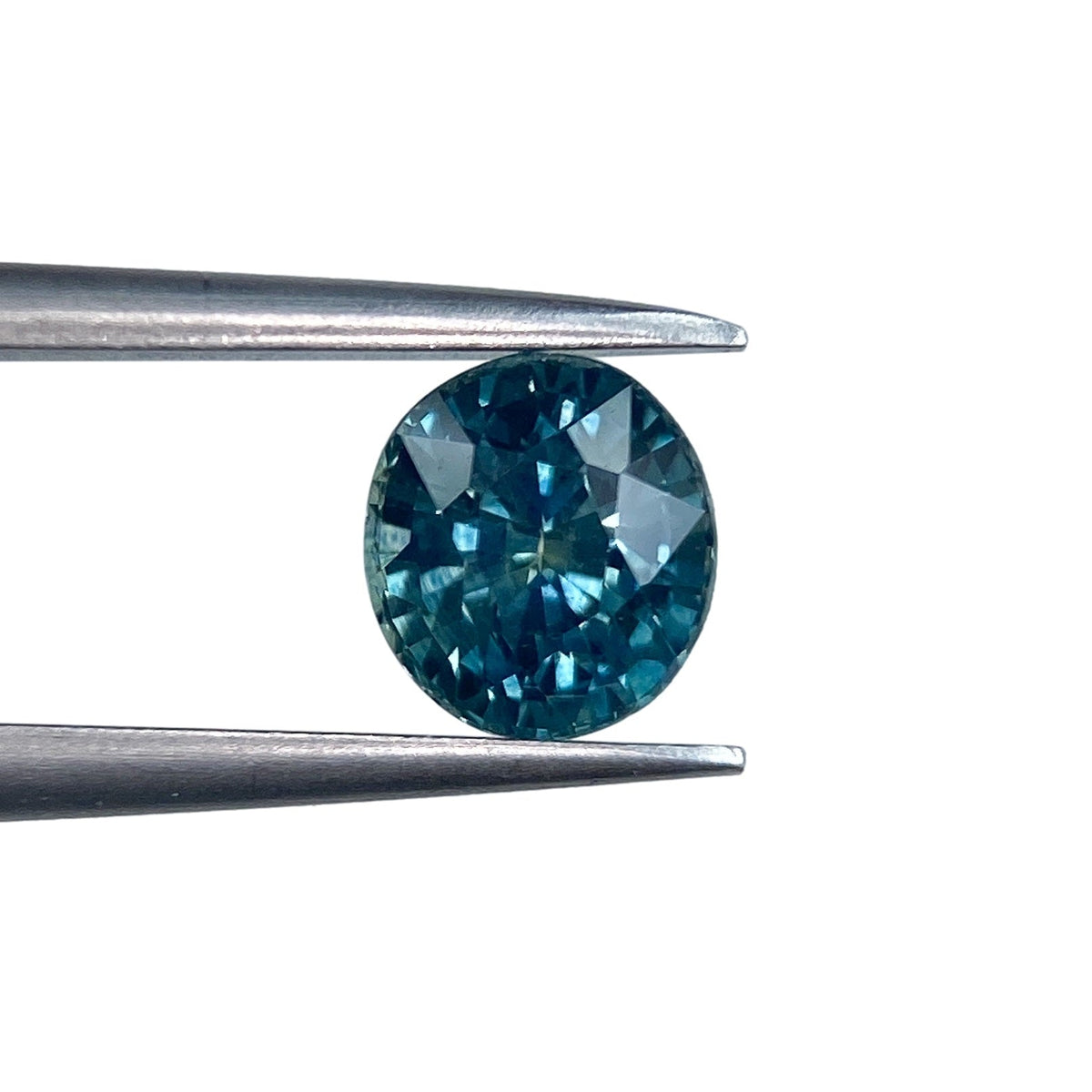 1.04ct oval brilliant cut blue Montana sapphire held by metal tweezers against a white background.