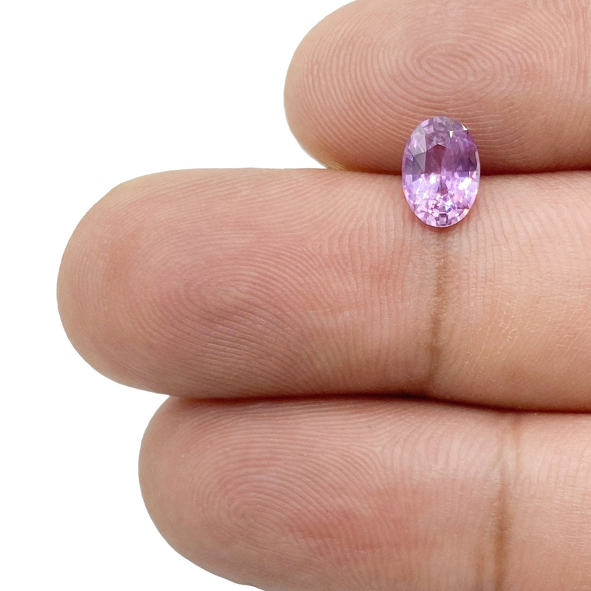 1.04ct oval brilliant cut violet sapphire held between fingers, showcasing its vibrant purple hue and faceted sparkle.