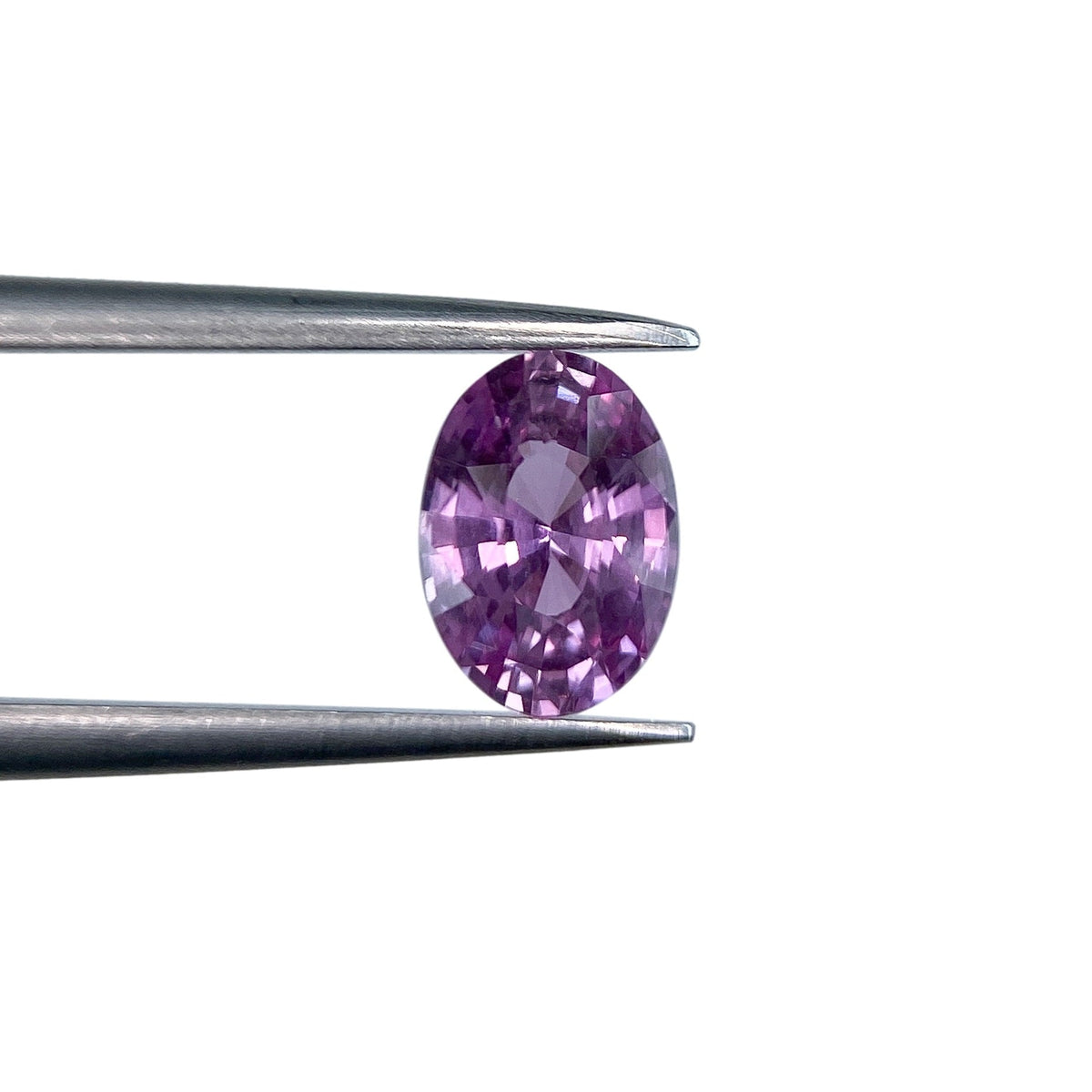 1.04ct oval brilliant cut violet sapphire held by metal tweezers against a white background.