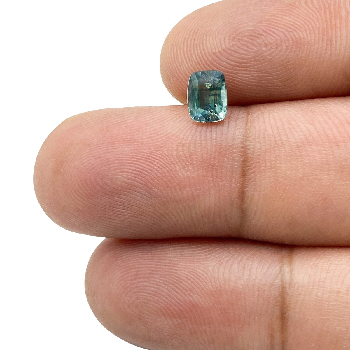 1.05ct brilliant cut cushion-shaped green Montana sapphire held between two fingers.