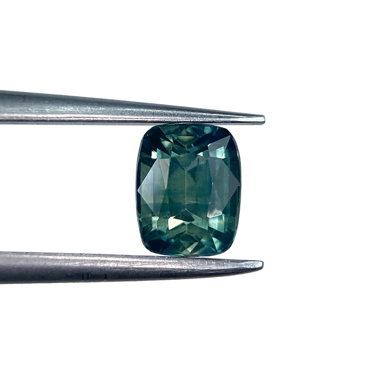 1.05ct cushion-cut green Montana sapphire with a brilliant facet pattern held in metal tweezers.