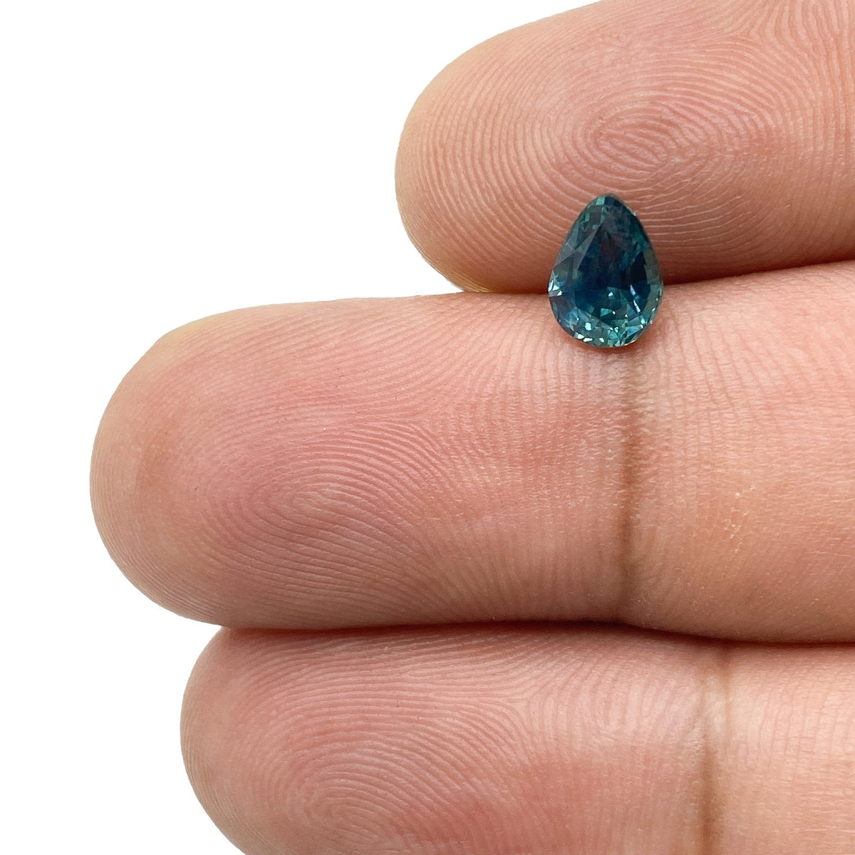1.05ct pear-shaped blue Montana sapphire with a brilliant cut held between fingers.