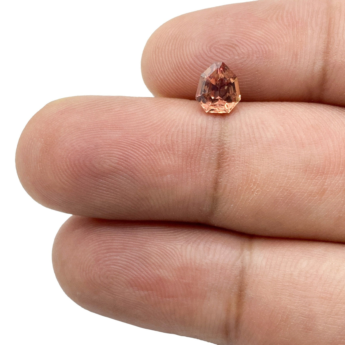 1.06ct brilliant cut brown sapphire with a unique shield shape held between fingers.