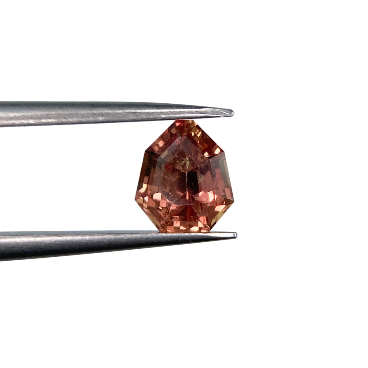 1.06ct brilliant cut brown sapphire in a unique shield shape held by metal tweezers against a white background.