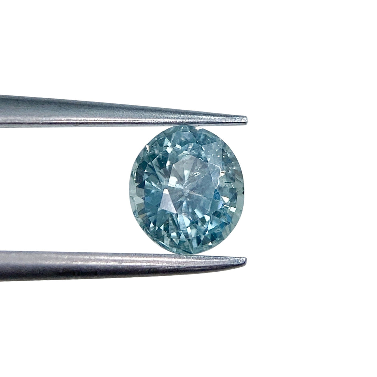 1.07ct oval brilliant cut blue Montana sapphire held in metal tweezers against a white background.