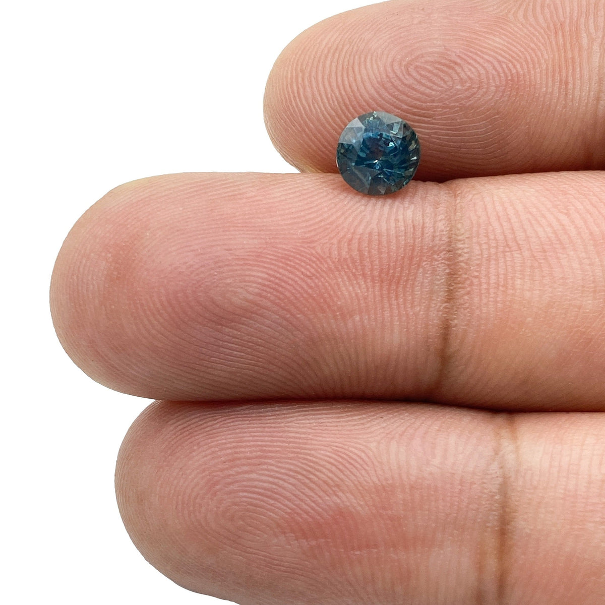 1.07ct round brilliant cut blue Montana sapphire held between two fingers.