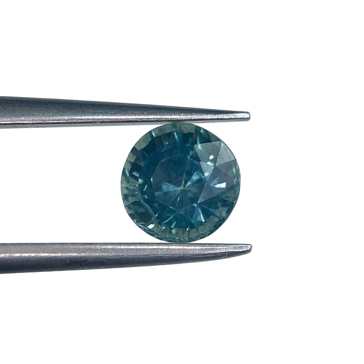 1.07ct round brilliant cut blue Montana sapphire held in metal tweezers against a white background.