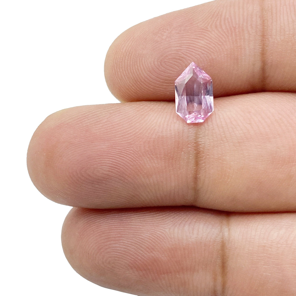 1.07ct brilliant cut pink sapphire with a unique shield shape held between two fingers.
