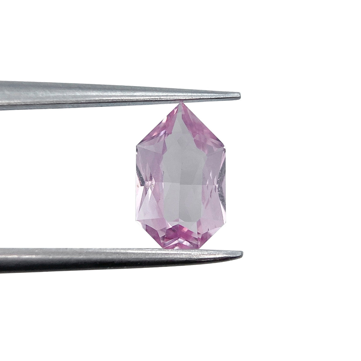 1.07ct brilliant cut pink sapphire in a unique shield shape held by metal tweezers against a white background.