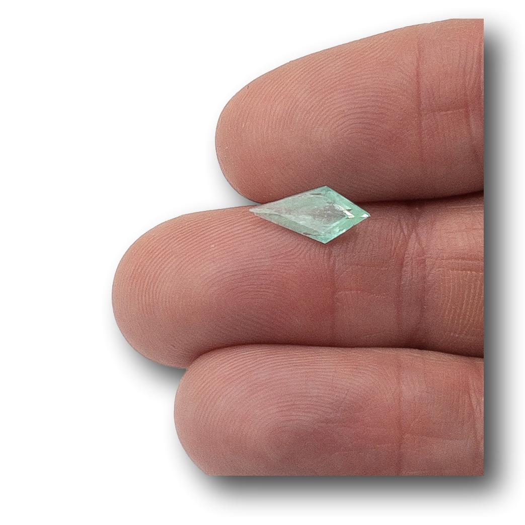 1.08ct kite-shaped Muzo emerald with a step cut, held between fingers to show its vibrant green color and unique geometry.