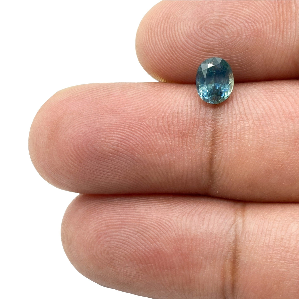 1.09ct brilliant cut oval blue Montana sapphire held between fingers, showcasing natural color and faceted sparkle.