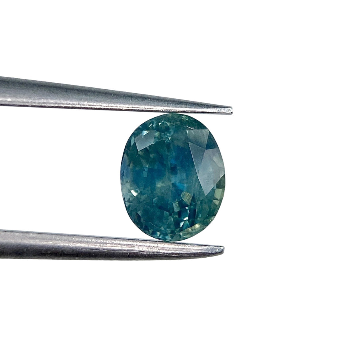 1.09ct oval brilliant cut blue Montana sapphire held in metal tweezers against a white background.