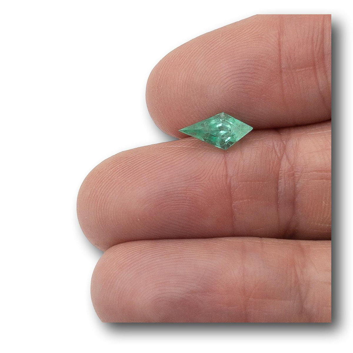 1.13ct kite-shaped Muzo emerald with a step cut held between fingers, showcasing its vibrant green color and geometric design.
