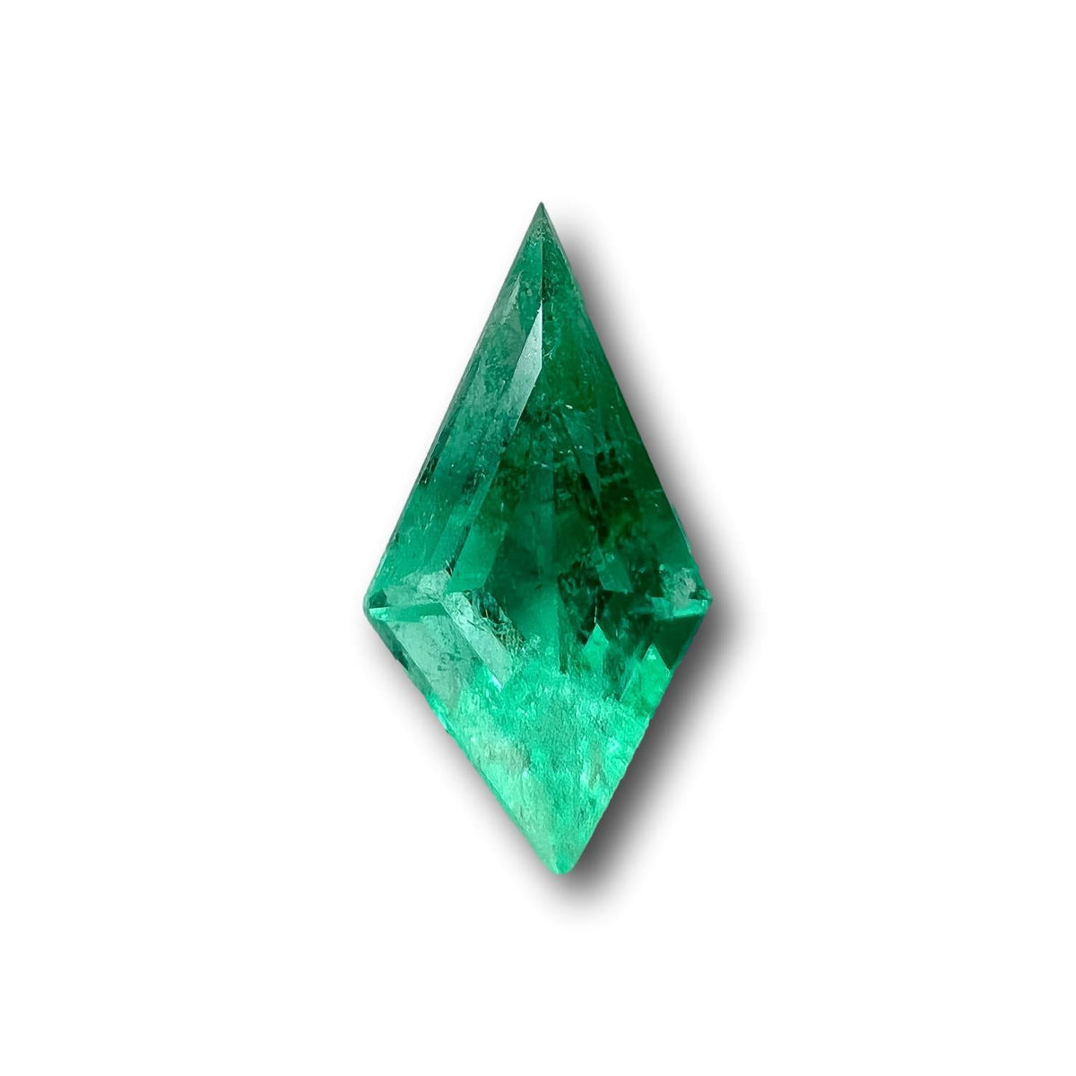 1.13ct Muzo Colombian emerald with a unique step-cut kite shape and vibrant green color on a white background.